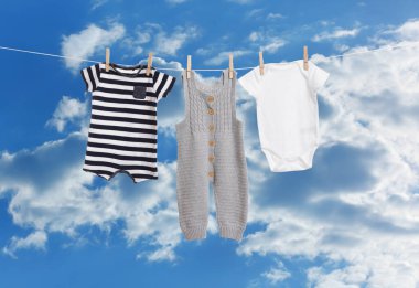 Mavi gökyüzüne karşı çamaşır ipinde kurumuş farklı bebek kıyafetleri.