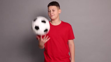 Gri arka planda futbol topu olan genç bir çocuk.