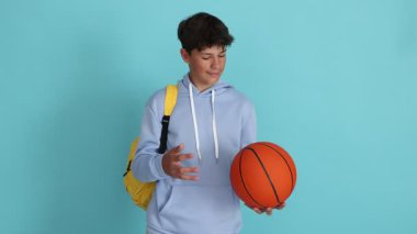 Açık mavi arka planda basketbol topu olan genç bir çocuk.