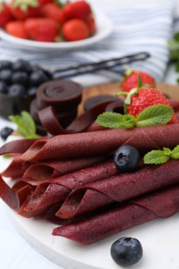 Lezzetli meyve dürümleri, çilekler, yaban mersini ve nane şekeri beyaz masada, yakın plan.