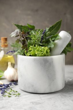 Topuzlu havan, farklı aromatik otlar ve baharatlar gri masada, yakın plan.