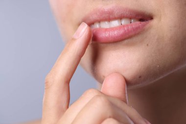 Açık gri arka planda dudak merhemi olan genç bir kadın, yakın plan.