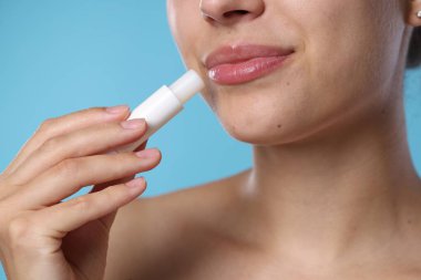 Açık mavi arka planda dudak merhemi olan genç kadın, yakın plan.