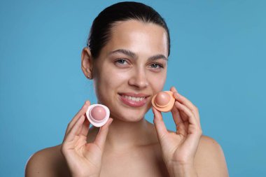 Açık mavi arka planda dudak kremleri olan genç bir kadın.