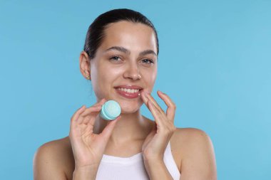 Açık mavi arka planda dudak merhemi olan genç bir kadın.