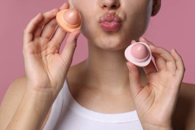 Pembe arka planda dudak merhemi olan genç bir kadın, yakın plan.