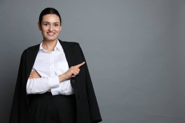 Takım elbiseli kendine güvenen iş kadını gri arka plandaki bir şeyi işaret ediyor. Metin için boşluk