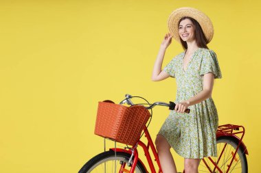Şapkalı gülümseyen kadın, açık yeşil arka planda sepeti olan bisikletli poz veriyor. Metin için boşluk