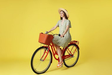 Açık yeşil arka planda sepeti olan şapkalı, gülen bir kadın.