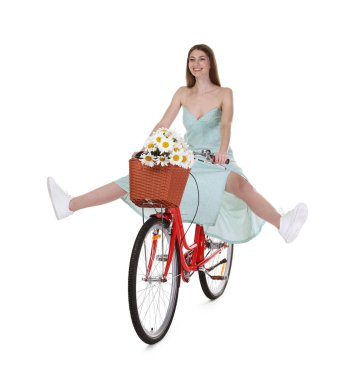 Gülen kadın, beyaz arka planda çiçek dolu bir sepetle bisiklet sürüyor.