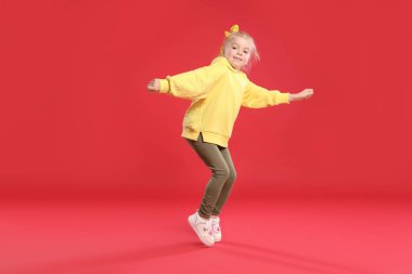 Kırmızı arka planda dans eden tatlı küçük kız.