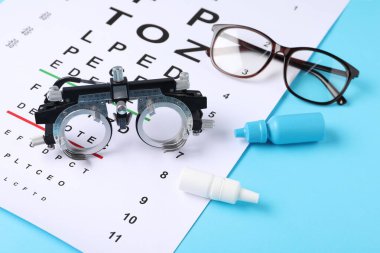 Görüş testi tablosu, gözlükler, deneme çerçevesi ve açık mavi arka planda tıbbi damlalar.