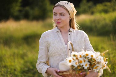 Açık havada sepet dolusu kır çiçeğiyle mutlu bir kadın.