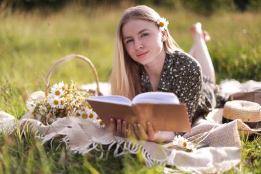 Bir buket kır çiçeğiyle çayırda kitap okuyan güzel bir kadın.