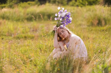 Bir buket kır çiçeğiyle güzel bir kadın çayırda güneşli bir günün tadını çıkarıyor.