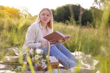Bir buket kır çiçeğiyle çayırda kitap okuyan bir kadın.