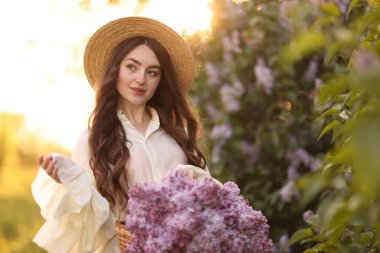 Güzel bir kadın, sabah çalıların yanında bir sepet leylak çiçeği taşıyor.