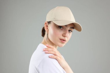 Gri arka planda şık beyzbol şapkalı güzel kadın, yakın plan.