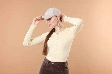 Beyzbol şapkalı güzel bir kadın bej arka planda poz veriyor.