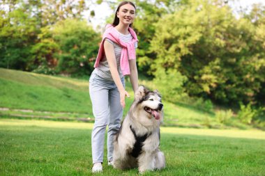 Yeşil çimlerin üzerinde sevimli Alaska köpeğiyle gülümseyen kadın.