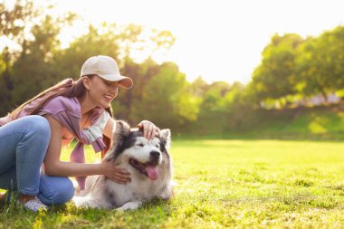 Gülümseyen bir kadın, Alaska 'lı köpeğini çimlerin üzerinde okşuyor. Metin için boşluk