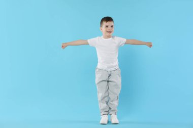 Mutlu küçük çocuk açık mavi arka planda dans ediyor