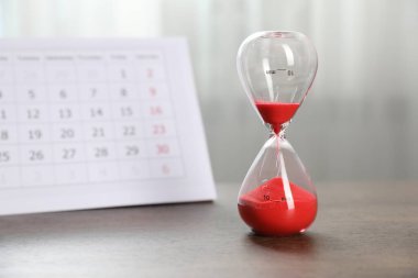 Son teslim tarihi. Kapalı alanda ahşap masada kum ve takvim akan kum saati.