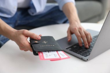 Pasaportu ve uçuş biletleri olan bir adam masadaki bilgisayarı kullanıyor, yakın plan.