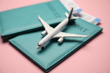 Biletli pasaportlar ve pembe arka planda uçak modeli, yakın plan.