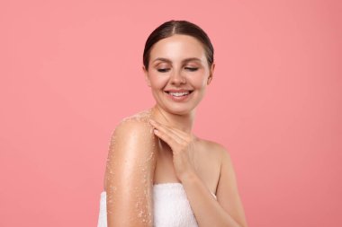 Gülümseyen kadın omuzlarını pembe arka planda ovalıyor.