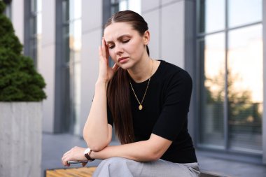 Ofis binasının dışındaki bankta oturan yorgun iş kadını.