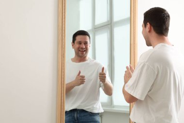 Aynanın yanında baş parmağını gösteren yakışıklı bir adam, metin için boşluk.