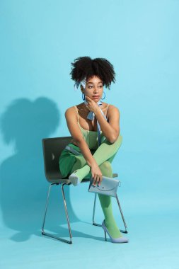 Açık mavi arka planda şık giyinmiş güzel Brezilyalı bir kadının moda portresi.