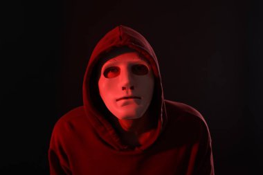 Anonimlik. Koyu arkaplanda kırmızı ışığı olan maskeli adam.