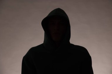 Gri arka planda kapüşonlu isimsiz bir adamın silueti.