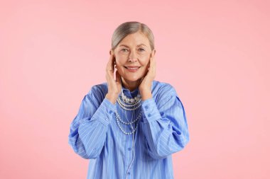 Kulaklıklı yaşlı kadın pembe arka planda müzik dinliyor.