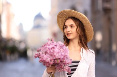 Bulanık arka planda bir demet leylak çiçeğiyle şapkalı gülümseyen kadın. Metin için boşluk