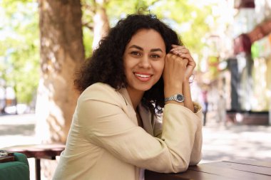 Açık hava kafede gülümseyen Latin Amerikalı kadının portresi.