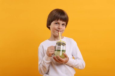 Turuncu arka planda limonata içen şirin bir çocuk. Tazeleyici içecek.