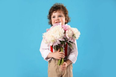Açık mavi arka planda bir buket güzel şakayığı olan sevimli küçük bir çocuk.