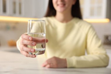 Mutfaktaki masada bir bardak su içen kadın, seçici bir odak noktası.