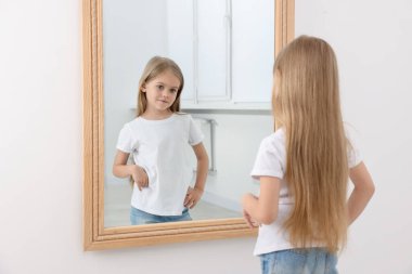 Üzgün küçük kız aynada kendine bakıyor.