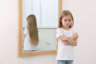 Evdeki aynanın yanındaki üzgün küçük kız.