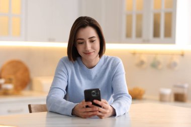 Mutfaktaki masada modern akıllı telefon kullanan bir kadın.