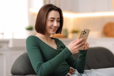 Evdeki koltukta modern akıllı telefon kullanan bir kadın.