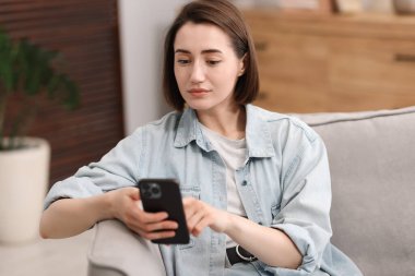 Evdeki koltukta modern akıllı telefon kullanan bir kadın.