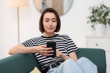 Evdeki koltukta modern akıllı telefon kullanan bir kadın.