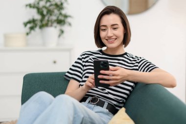 Evdeki koltukta modern akıllı telefon kullanan bir kadın. Metin için boşluk