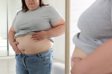 İçeride aynanın yanında göbeği aşırı yağlı bir kadın, yakın plan. Aşırı kilolu