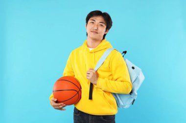 Basketbol topu ve açık mavi arka planda sırt çantası olan öğrenci.